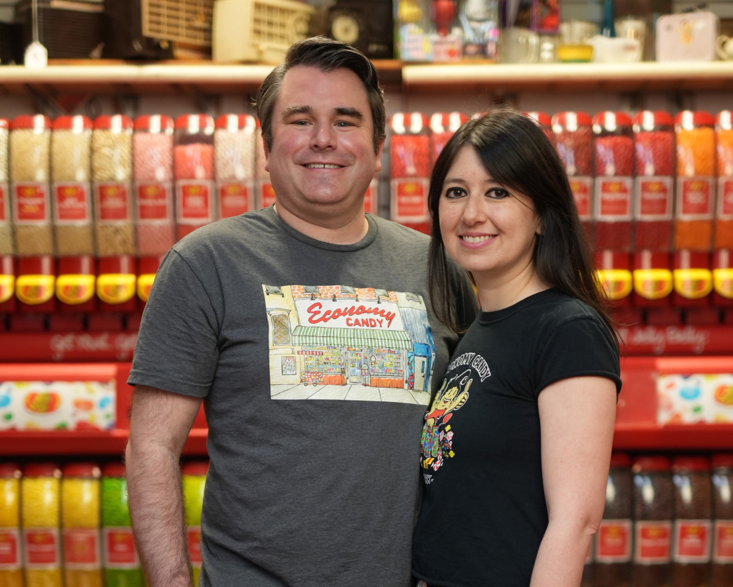 Les propriétaires d’Economy Candy posent dans leur boutique et portent des t-shirts Economy Candy.