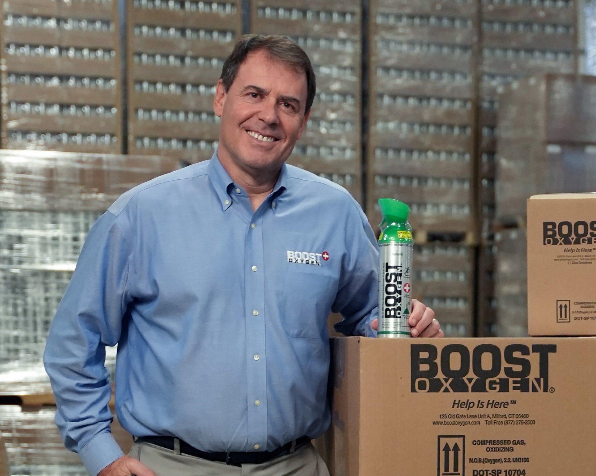Le propriétaire de Boost Oxygen pose dans un entrepôt avec un produit Boost Oxygen.