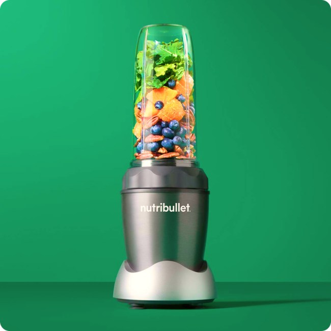 Un mixeur Nutribullet rempli de fruits et légumes sur fond vert.